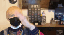 a person wearing a black mask is standing in front of a sign that says shots
