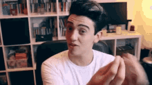 a man in a white shirt is making a funny face while sitting in front of a bookshelf .