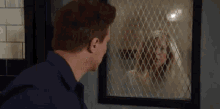 a man and a woman are looking at each other through a fenced in window .