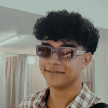 a young man with curly hair wearing purple sunglasses