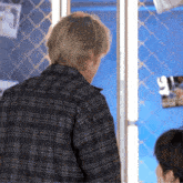 a man in a plaid shirt is standing in front of a window