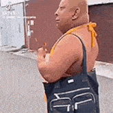 a shirtless man is standing on a sidewalk holding a black bag .