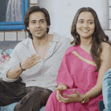 a man and a woman are sitting on a couch and the woman is wearing a pink dress