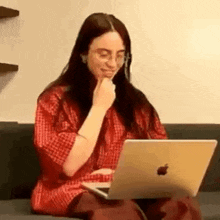 billie eilish is sitting on a couch with a laptop .