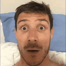 a man with a surprised look on his face is laying in bed