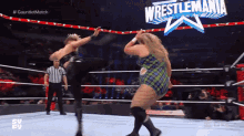 two women are wrestling in a ring with a sign that says wrestlemania on it