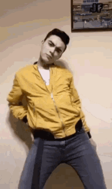 a man wearing a yellow jacket and blue jeans is dancing in front of a wall .