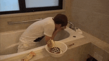 a man washing his face in a bathtub next to a bucket of food