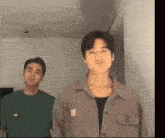 two men are standing next to each other in a room and one of them is wearing a green shirt .