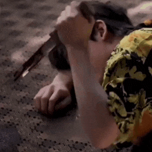 a man in a floral shirt is laying on the floor holding a knife .