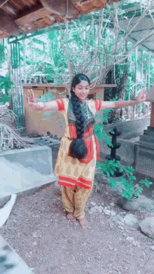a girl in a yellow and red dress is standing in front of a tree with her arms outstretched