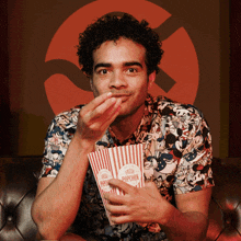 a man wearing a mickey mouse shirt is eating popcorn