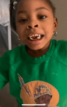 a little girl is wearing a green shirt with a picture of a man on it and has white teeth .