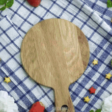a round wooden cutting board is on a blue and white checkered cloth