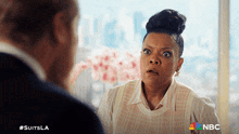 a woman with a surprised look on her face is talking to a man in a suit with the nbc logo in the corner