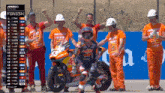 a man on a motorcycle stands in front of a group of men wearing orange shirts with the word finish on them