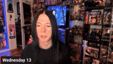 a man with long black hair is sitting in front of a television with the date wednesday 13 on the bottom