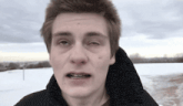 a young man with braces on his teeth looks at the camera in front of a snowy field