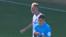 a man in a white shirt is walking on a soccer field with another man .