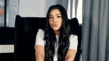 a woman with long hair is sitting in a chair blowing a kiss .