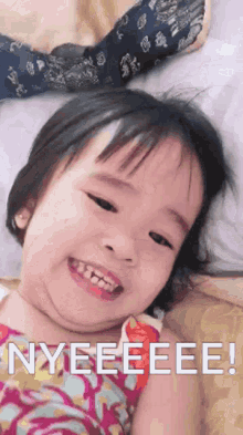 a little girl is smiling and laying on a bed with the words nyeeeee written on the bottom