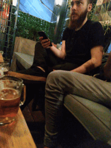 a man with a beard sits at a table with a glass of beer in front of him