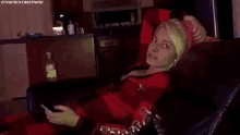 a woman is sitting on a couch holding a cell phone and a bottle of alcohol .