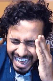 a man with curly hair and a beard is laughing with his hand on his forehead