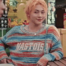 a young man wearing a striped sweater is sitting at a table .