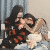 two women are sitting next to each other on a couch with a stuffed cat .