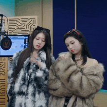 two women wearing fur coats are standing in front of a microphone