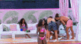 a group of people are standing around a pool while a woman in a bikini is dancing .
