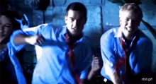a group of people in blue shirts and ties are dancing in a dark room ..