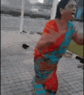 a woman in a red and blue saree is dancing on the sidewalk