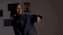 a woman in a blue sweatshirt is dancing in front of a wall of pictures