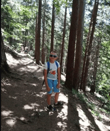a young boy wearing sunglasses and a shirt that says hawaii is standing on a path in the woods