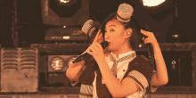 a woman singing into a microphone wearing a top hat