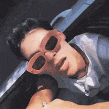 a man wearing pink sunglasses is laying in a car .