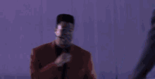 two men are singing into microphones in front of a crowd in a dark room .
