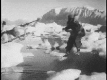 a black and white photo of a man standing on ice with mountains in the background