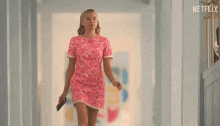 a woman in a pink dress is walking down a hallway with a netflix logo on the wall behind her