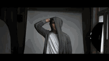 a man wearing a hoodie and a white shirt is standing in front of a white wall .