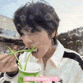 a young man is eating noodles from a cup with a pink sticker that says bibi y sakuppang