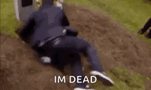 a man is laying in the dirt next to a grave and says `` im dead '' .