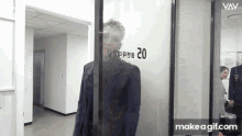 a man in a suit is standing in front of a glass door with the number 20 written on it .