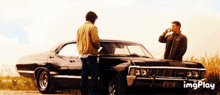 two men are standing in front of a black car with a license plate that says ecj
