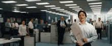 a man in a white shirt is holding a large piece of paper in an office