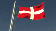a red and white flag with a cross on it is flying in the wind