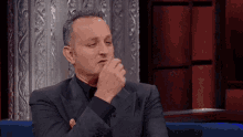 a man in a suit is sitting on a blue couch with his hand on his chin .