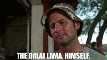 a man wearing a bucket hat is standing in front of a building and says `` the dalai lama , himself . ''